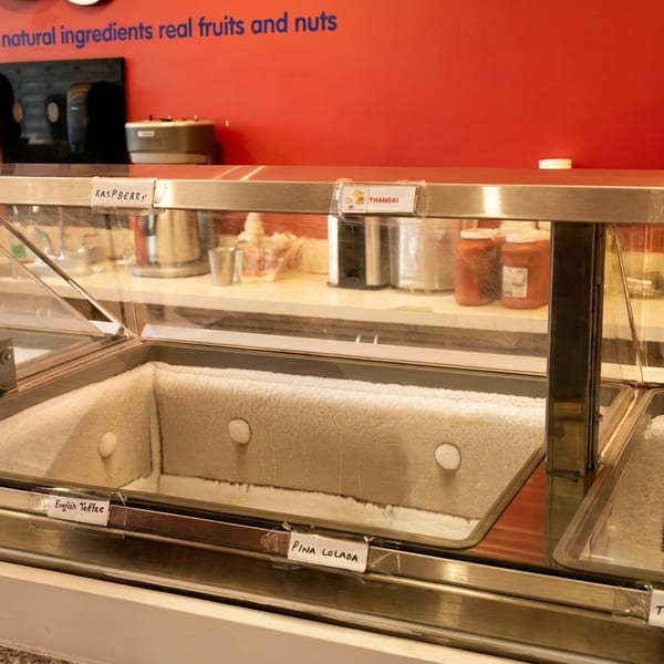 Empty, frosted dessert display case with flavor labels against a red wall.