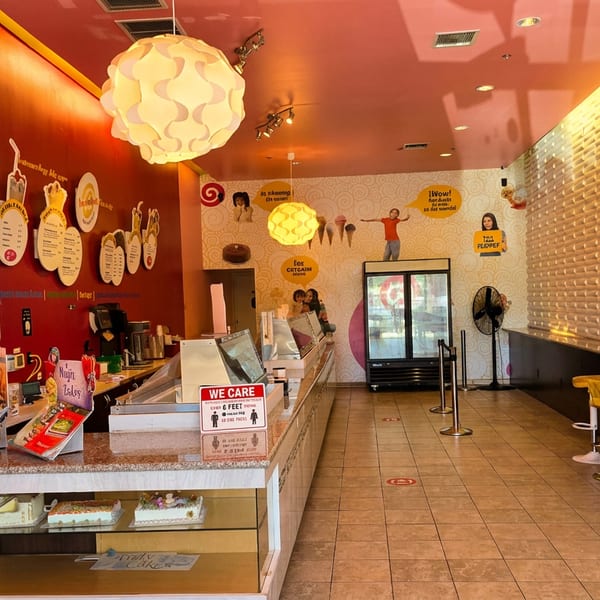 Brightly lit ice cream shop with a service counter, cake displays, and colorful bar stools.