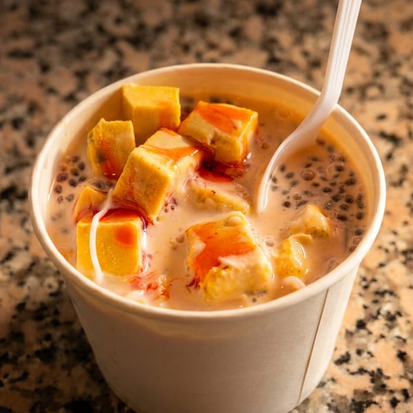 Creamy dessert with yellow cubes, red syrup, and black seeds in a cup, with a spoon.