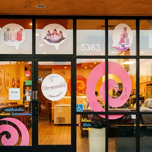 Storefront of Nirvanoah! Indian ice cream shop with window decals of desserts and pink spirals.