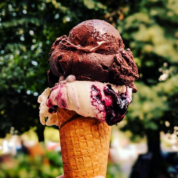 Two scoops of chocolate and berry swirl ice cream in a waffle cone outdoors.